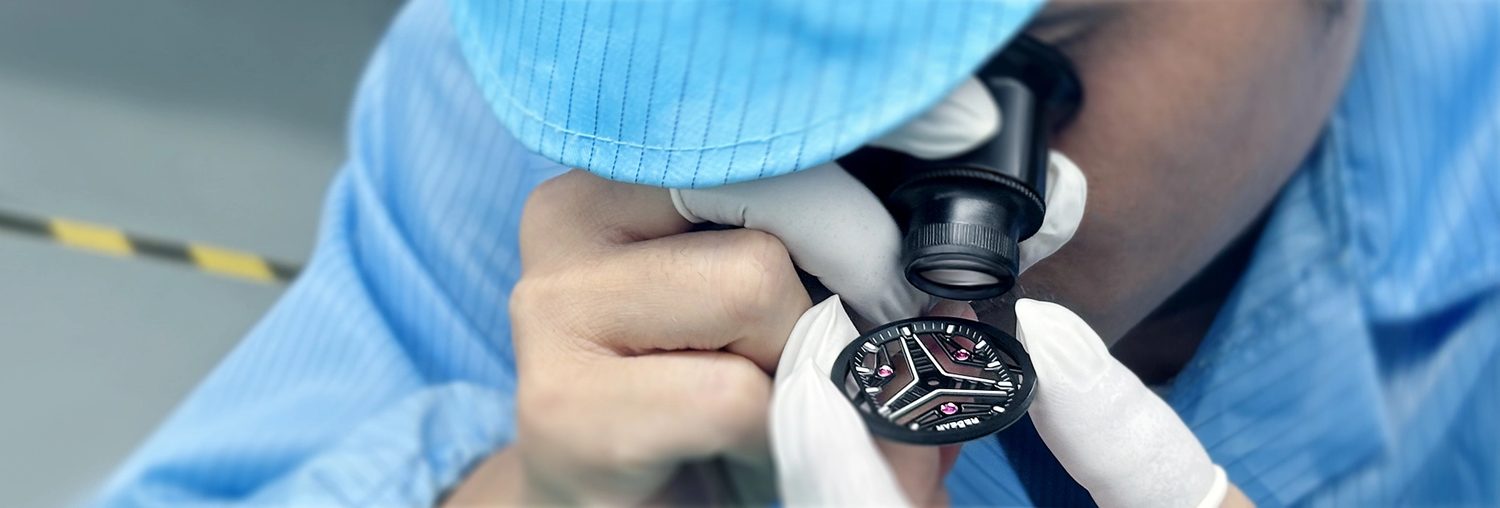 An operator working on a watch at the bench with a hand tool.
