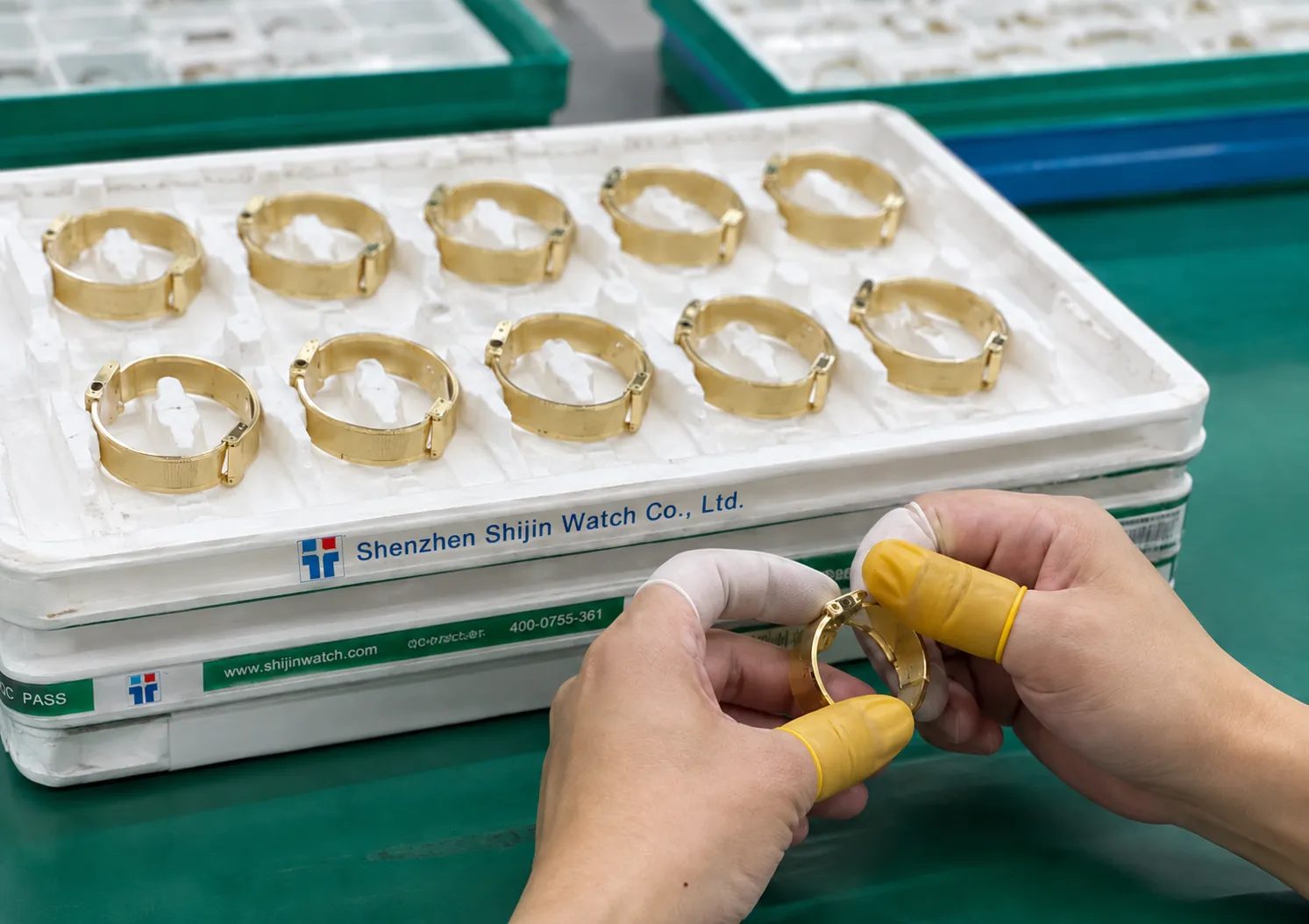 Gold cases in a tray marked Shenzhen Shijin Watch Co., Ltd, handled in finger cots at final inspection.