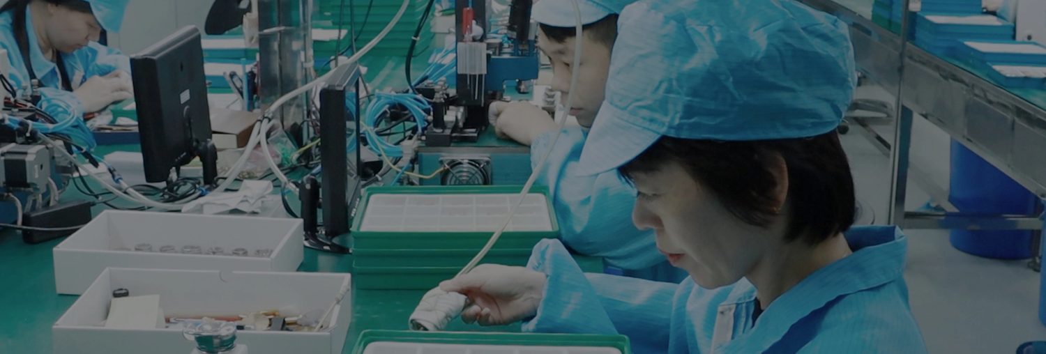 The production line, operators seated at benches in caps and coats.
